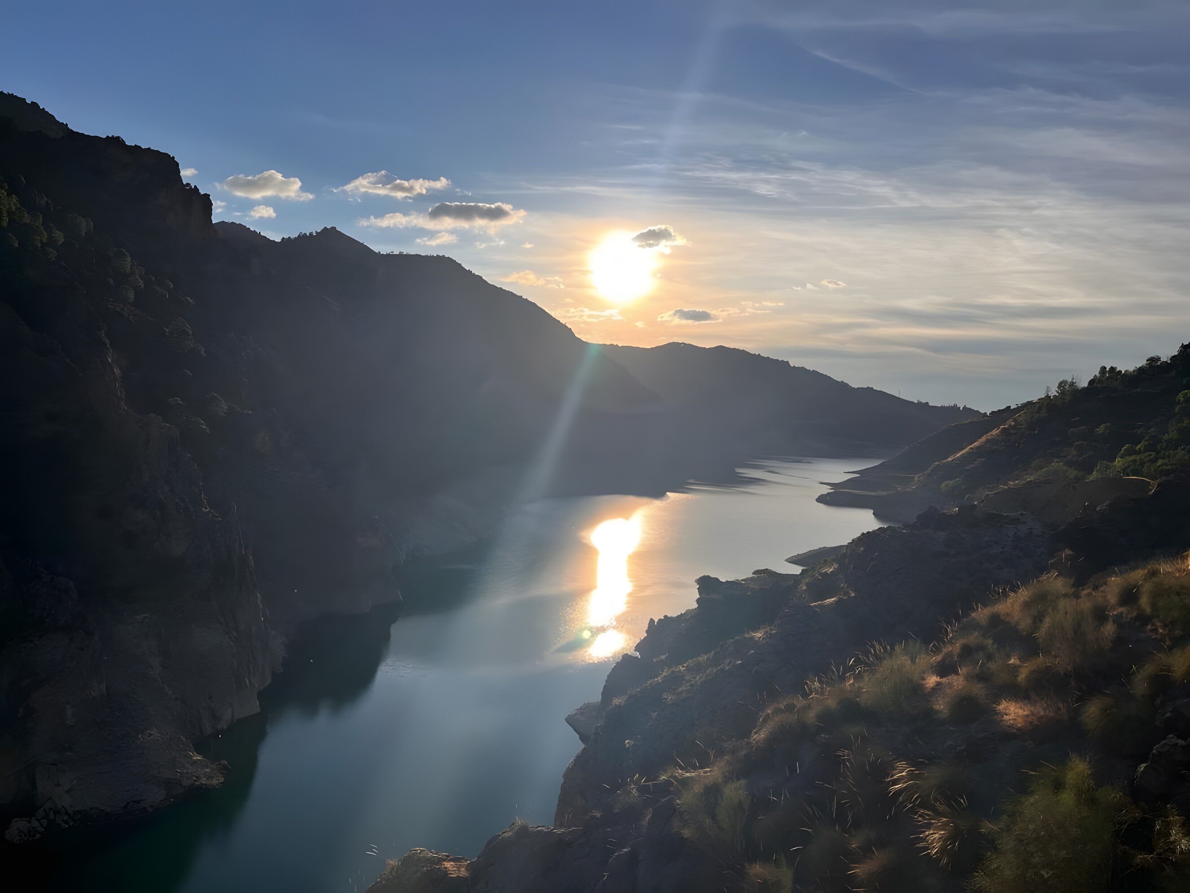 Un valle fluvial flanqueado por montañas, con el sol poniéndose tras ellas.
