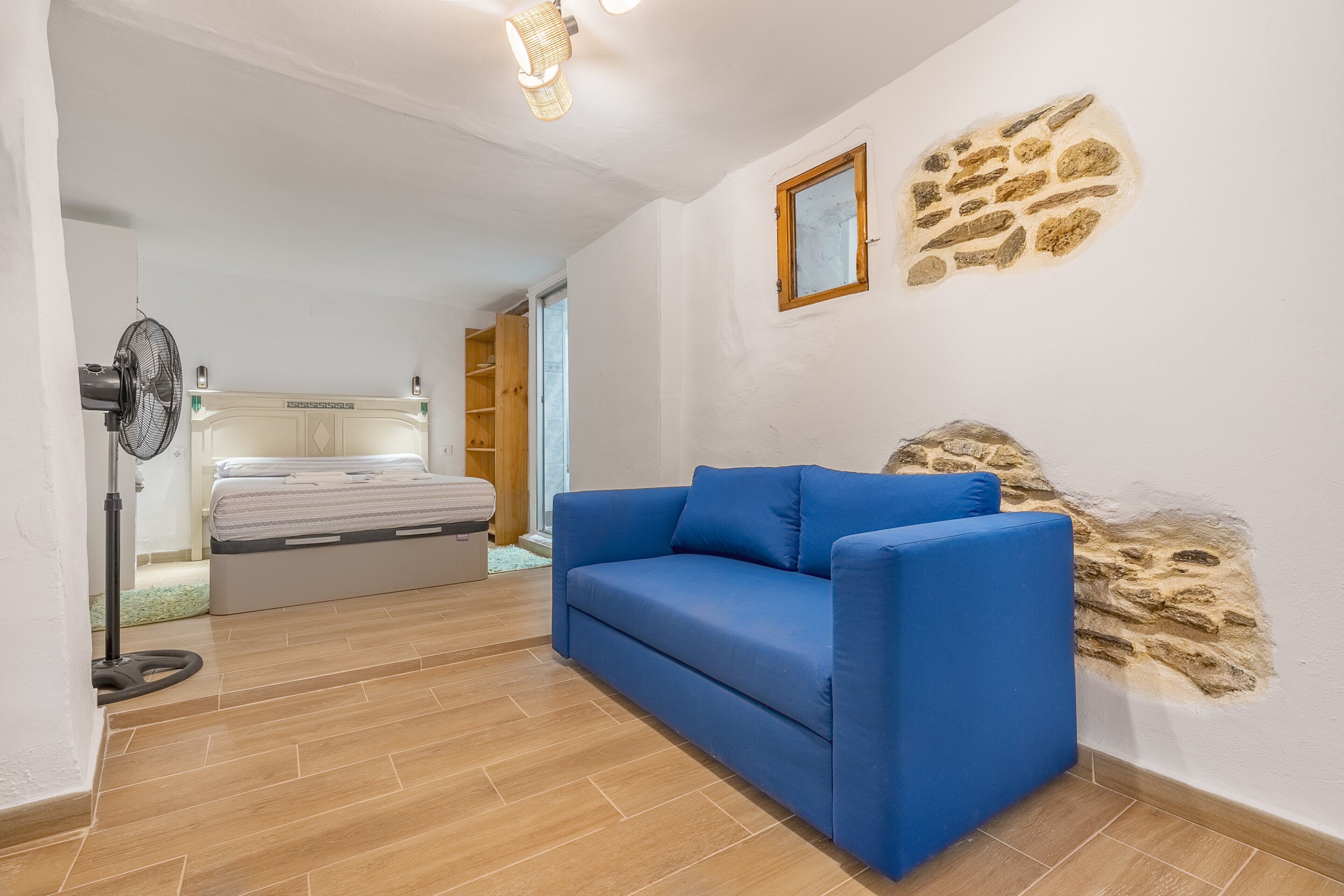 Ein Zimmer mit einem blauen Sofa, einem Bett, einem Ventilator und einer Wand mit Steinoptik.