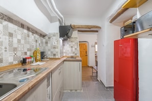 A kitchen with patterned tiles, a wooden countertop, a red refrigerator, and a wooden door leading to another room.
