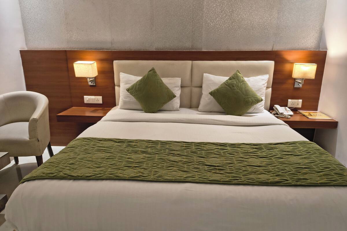 Une chambre d’hôtel avec un lit, deux tables de chevet, une chaise et un téléphone fixé au mur.