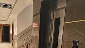 A modern elevator with a marble wall, a fire exit sign, and a no smoking sign. - Hotel Aman Suites at IGI by Arch Group (New Delhi)