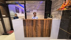 A reception desk with a wooden front panel, a white chair in the foreground, and a marble wall with a 'No Smoking' sign. - Hotel Aman Suites at IGI by Arch Group (New Delhi)
