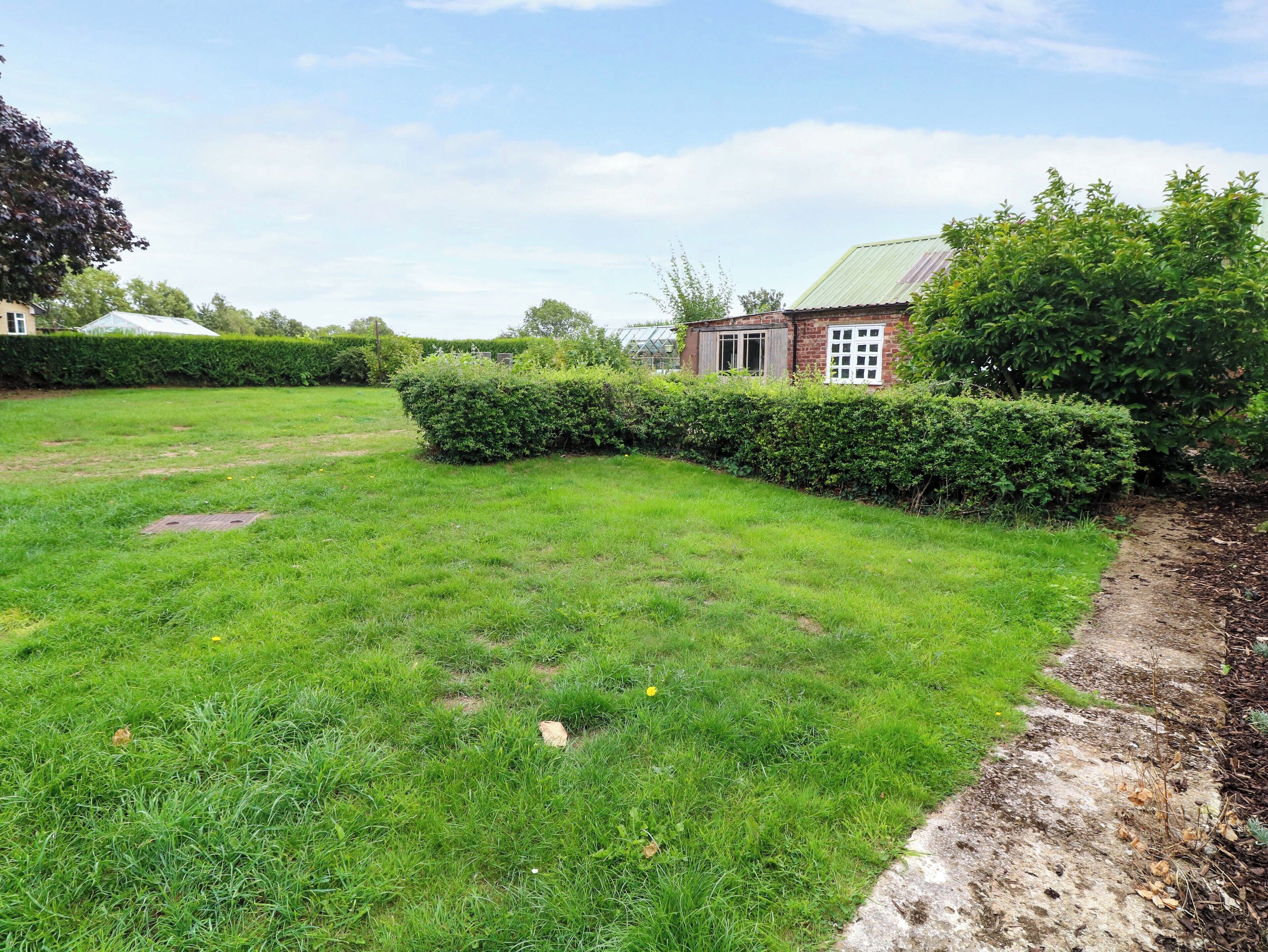 A grassy yard with a brick house, a hedge, and a path.