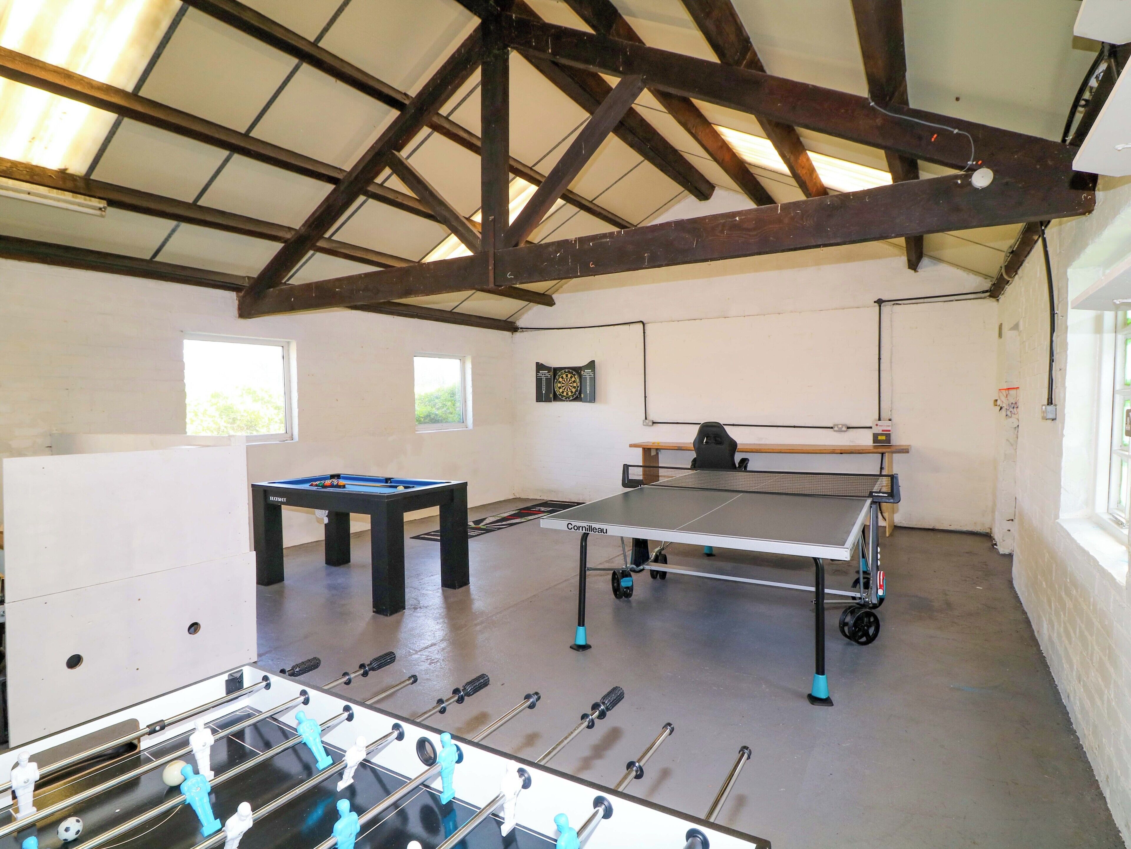 A room with a foosball table, ping pong table, and a dartboard.