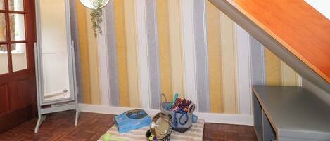 A room with striped wallpaper, a wooden sloped ceiling, a mirror, a pet bowl, a leash, and a basket.