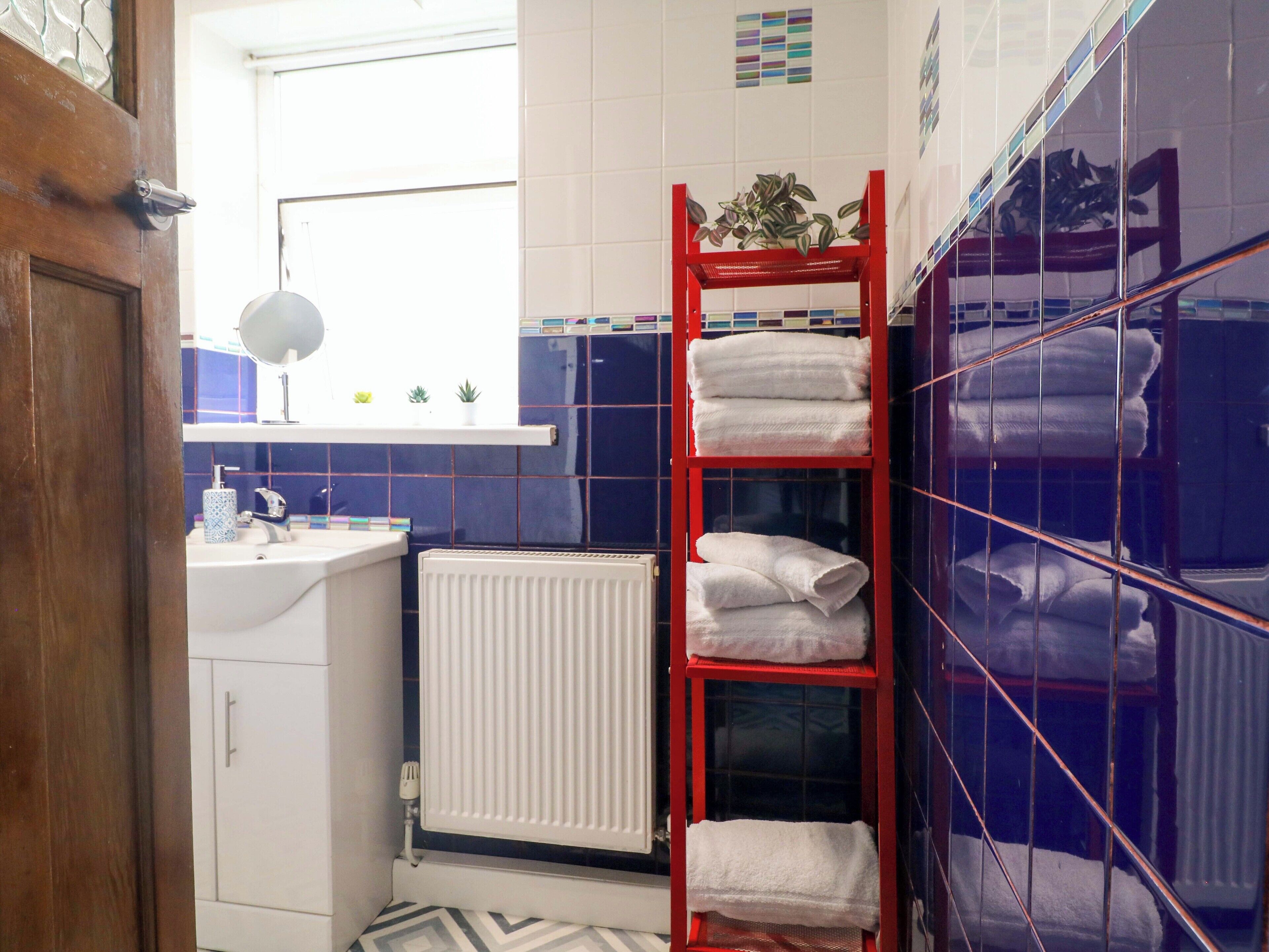 A bathroom with a white sink, a mirror, a red towel rack, and a radiator.