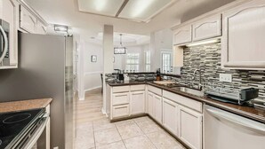 Una cocina moderna con armarios blancos, un refrigerador de acero inoxidable, una encimera negra y un salpicadero con diseño.
