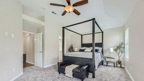 Un dormitorio con cama con dosel, ventilador de techo, mesita de noche, lámpara y planta en maceta.