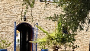An outdoor seating area with a round glass table and blue chairs, surrounded by potted plants and a stone wall. - Welcome to Villa Fatima - Your haven of tranquility (Ghazoua)
