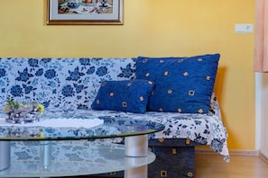 Un canapé recouvert d’un tissu à motifs floraux et géométriques, une table basse en verre et un tableau encadré accroché au mur.