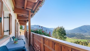 Un balcón de madera con una mesa y sillas, con vistas a un paisaje montañoso.
