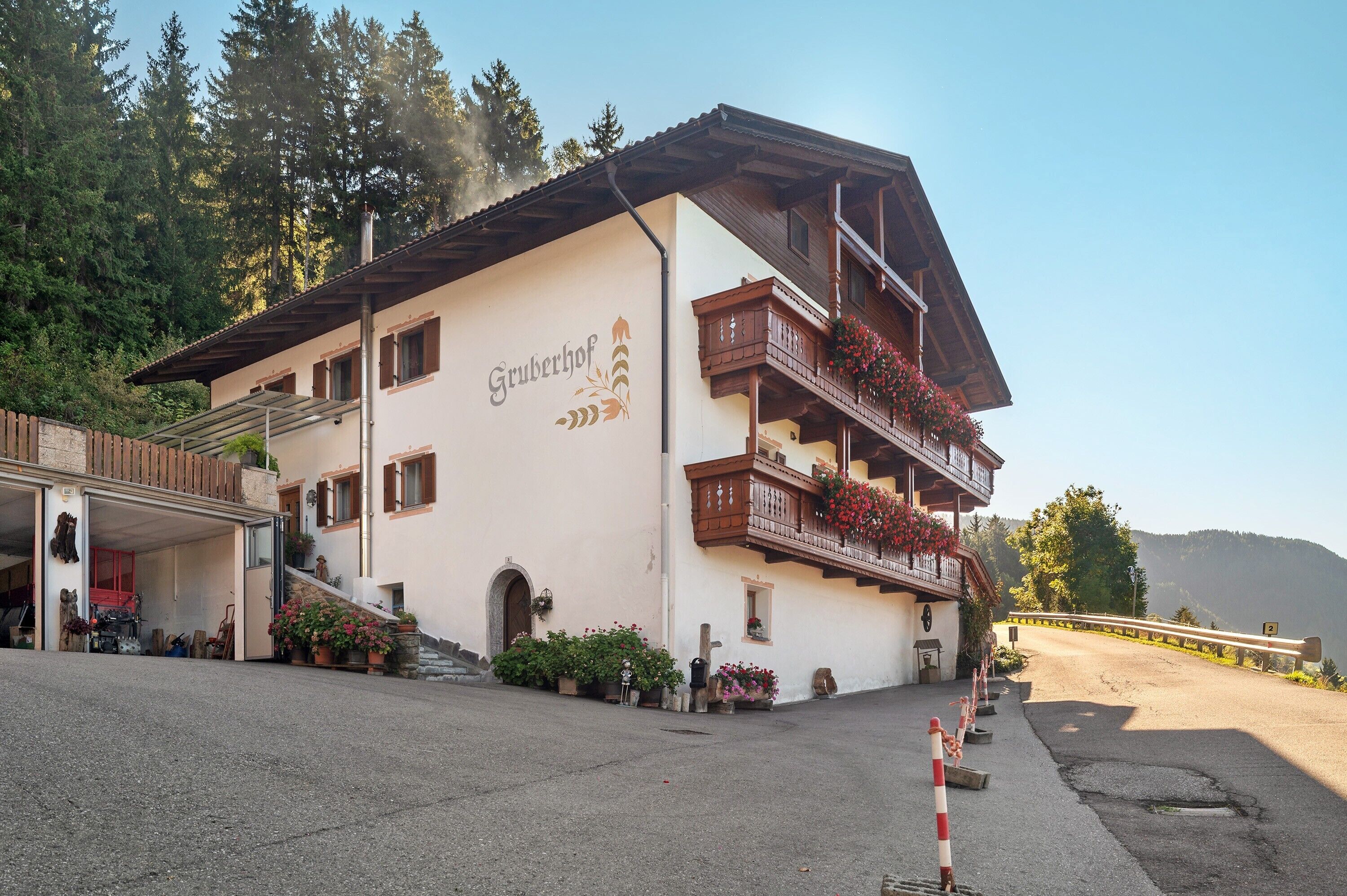 Ein Gebäude mit dem Schild 'Gruberhof', einem Balkon mit Blumen und einem Parkplatz.