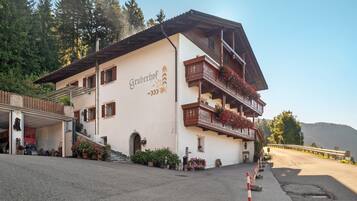 Ein Gebäude mit dem Schild 'Gruberhof', einem Balkon mit Blumen und einem Parkplatz.