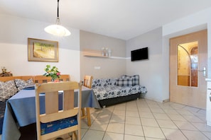 A dining area with a table, chairs, a sofa, a TV mounted on the wall, and a wooden door with a glass panel.