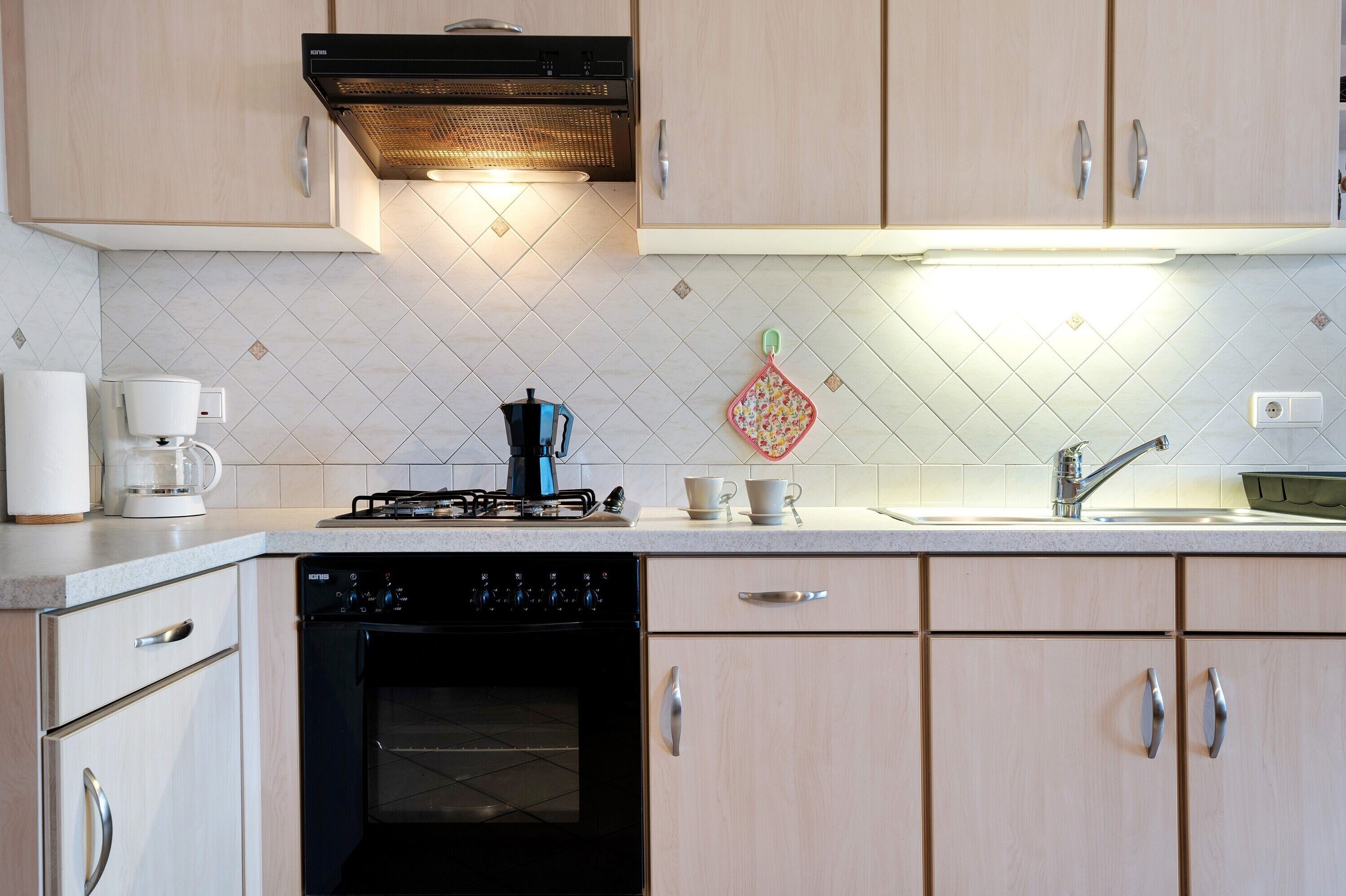 A modern kitchen with light wood cabinets, a gas stove, a coffee maker, and a dishwasher.
