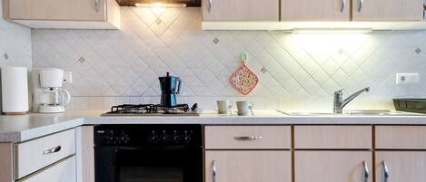 A modern kitchen with light wood cabinets, a gas stove, a coffee maker, and a dishwasher.