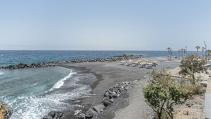 A coastal view with a rocky beach, a wooden pier, and a row of beach umbrellas. - 'Afirama 1' Holidays with Sea View, Wi-Fi and Air Conditioning (Las Caletillas)