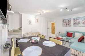 Un salon moderne comprenant un coin repas, un escalier et un tableau représentant un paysage urbain.