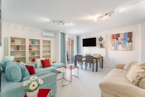 A modern living room with a sofa, coffee table, dining area, and a flat-screen TV mounted on the wall.