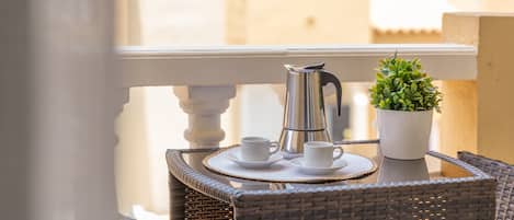A balcony with wicker furniture, a metal coffee pot, two white cups, and a small potted plant.