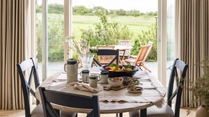 An open dining area with a table set for breakfast, featuring a bowl of fruit, a pitcher, and a vase with flowers. - Meadowside - Rock - stylish retreat sleeping up to 8 guests in 4 bedrooms (Rock)