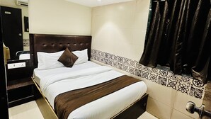 Een hotelkamer met een bed, een plafondventilator, een badkamer met douchegordijn en een betegelde muur.