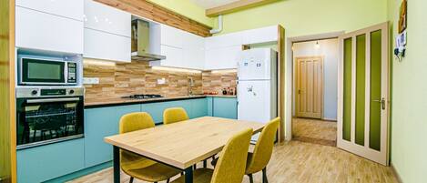 A compact kitchen with a wooden table and chairs, a microwave, oven, and a refrigerator.