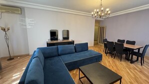 Una sala moderna con un sofá seccional, una mesa de centro, un comedor con sillas y una mesa, y una araña.