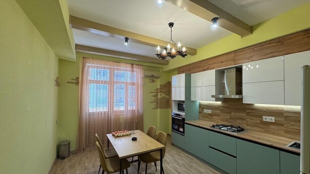 Una cocina compacta con zona de comedor, que incluye una mesa de madera, sillas y una araña.