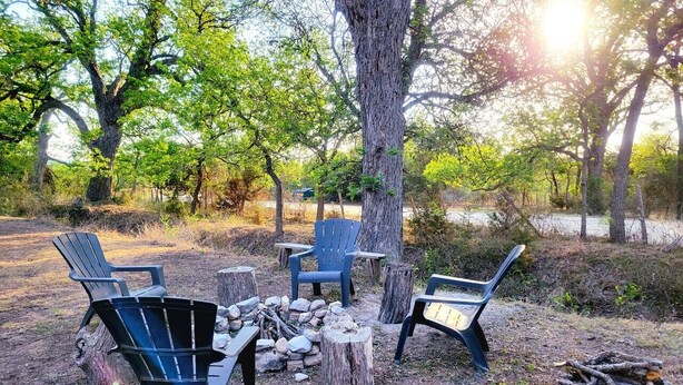 Un terrain de camping avec quatre chaises Adirondack disposées autour d’un foyer.