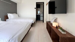 A hotel room with two beds, a TV mounted on the wall, a wooden bedside table with a lamp, and a small plant.