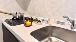 A kitchen with a stove, a pot, a candle, a sink, and a faucet.