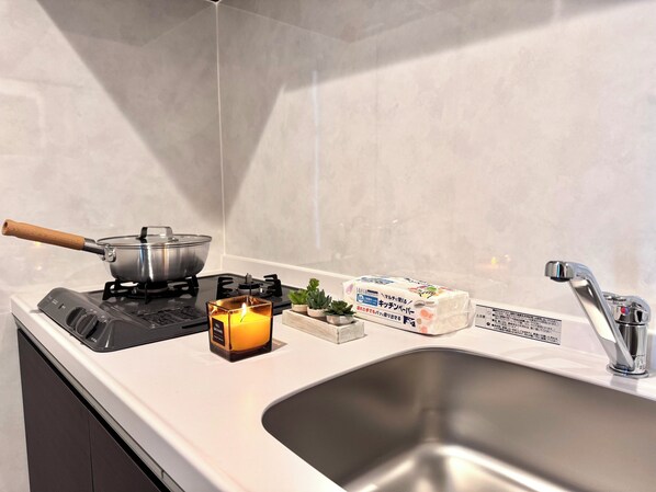 A kitchen with a stove, a pot, a candle, a sink, and a faucet.