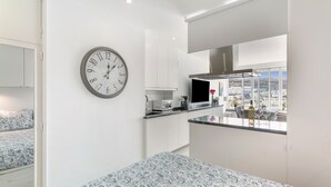 Eine moderne Küche mit weißen Schränken, einer Uhr und Blick auf die Stadt durch große Fenster.