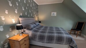 A bedroom with a bed, a nightstand, a lamp, a chair, and a wall with deer head decals. - Cozy one Bedroomed House in Aberchirder (Huntly)