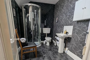 A bathroom with a glass shower enclosure, a toilet, a sink, and a chair. - Cozy one Bedroomed House in Aberchirder (Huntly)