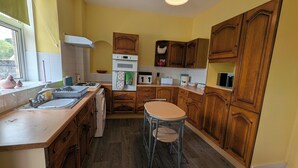 A kitchen with wooden cabinets, a sink, a stove, and a dining area with stools. - Cozy one Bedroomed House in Aberchirder (Huntly)