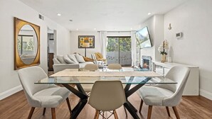 Un comedor moderno con una mesa de vidrio y cuatro sillas, un sofá, una chimenea y un espejo grande.