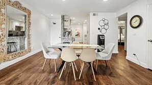 Un comedor con una mesa de vidrio, cuatro sillas, un espejo grande y un reloj en la pared.