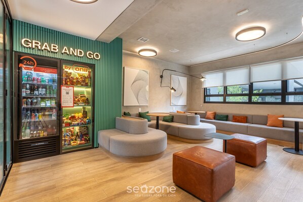 A modern lounge area with a 'Grab and Go' vending machine, seating arrangements, and large windows providing natural light. - Building With Swimming Pool and Gym in Pinheiros-sp - VBP (São Paulo)