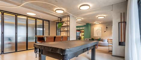 Een modern interieur met een biljarttafel, een groene bar en een zithoek met kussens.