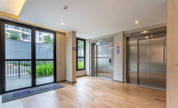 A modern elevator area with two elevators, a wooden floor, and a glass door leading outside. - Building With Swimming Pool and Gym in Pinheiros-sp - VBP (São Paulo)