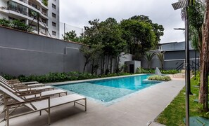 A swimming pool with lounge chairs, surrounded by greenery and a grey building. - Building With Swimming Pool and Gym in Pinheiros-sp - VBP (São Paulo)
