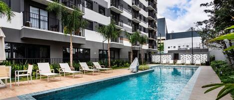 A modern hotel with a swimming pool, multiple balconies, and outdoor seating.