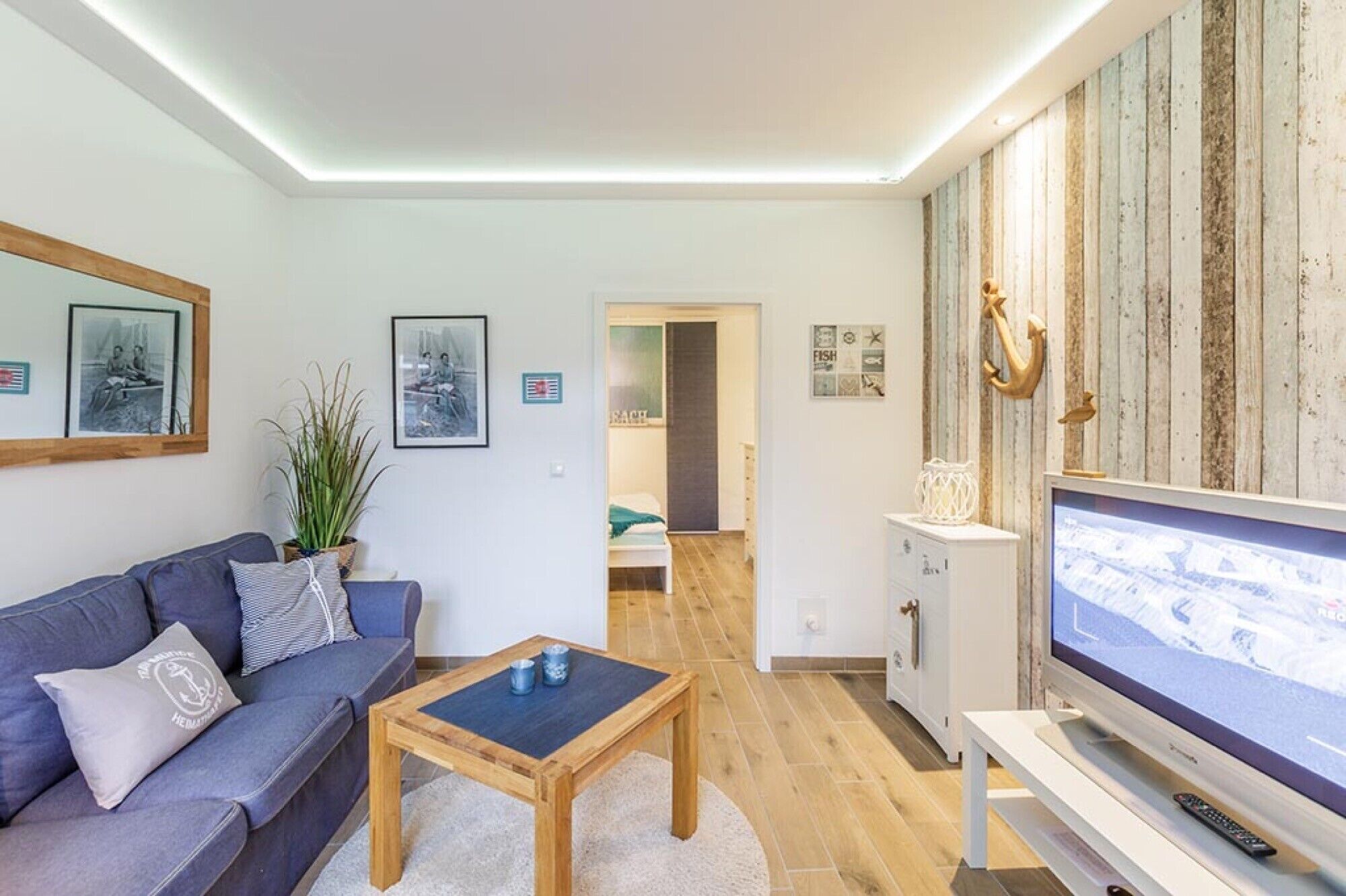 A modern living room with a sofa, coffee table, TV, and nautical decor.