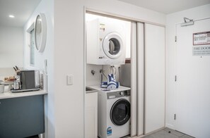 A laundry room with a washing machine, dryer, and a small countertop with a coffee machine and a bowl. - Villa Luxe On Airlie (Airlie Beach)