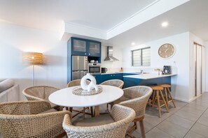 A modern kitchen with blue cabinets, a round dining table, wicker chairs, and a clock on the wall.