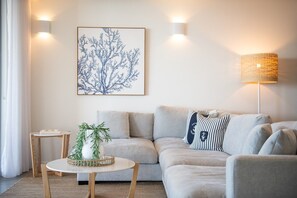 Ein Wohnzimmer mit grauem Sofa, einem runden Couchtisch, einer Wandlampe und einem gerahmten Kunstwerk.