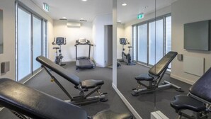 Un gimnasio con equipo de ejercicio, incluyendo cintas de correr y bancos de pesas, y amplias ventanas.