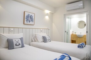 A hotel room with two beds, a framed artwork on the wall, a round mirror, and a bathroom with a sink and towel.